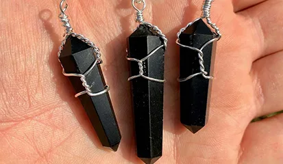 Three black onyx point pendants held in a hand